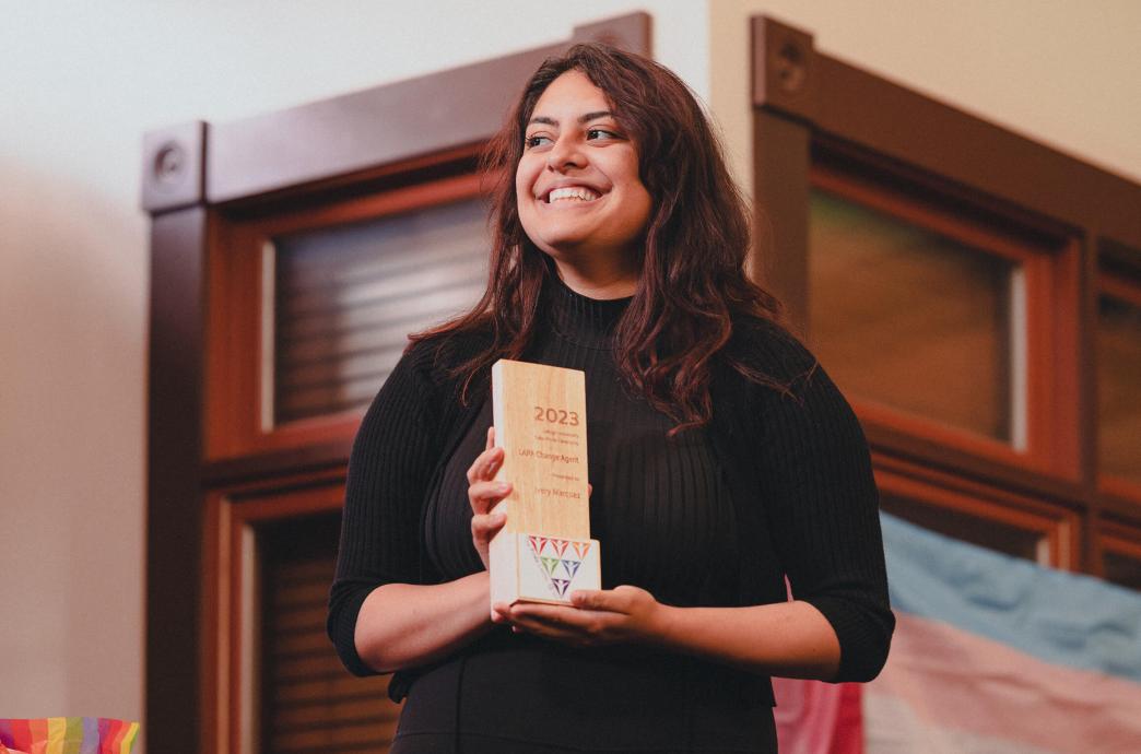 Student smiles while standing on a stage with an award for LAPAs Change Agent honor.