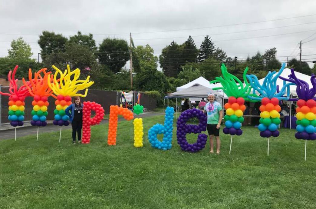 A large display of balloons on a green lawn spell out "Pride" at an outdoor event.
