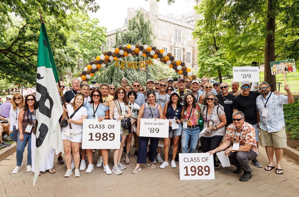 Class of 1989 poses with the white and green class flag and signs under the balloon arch.