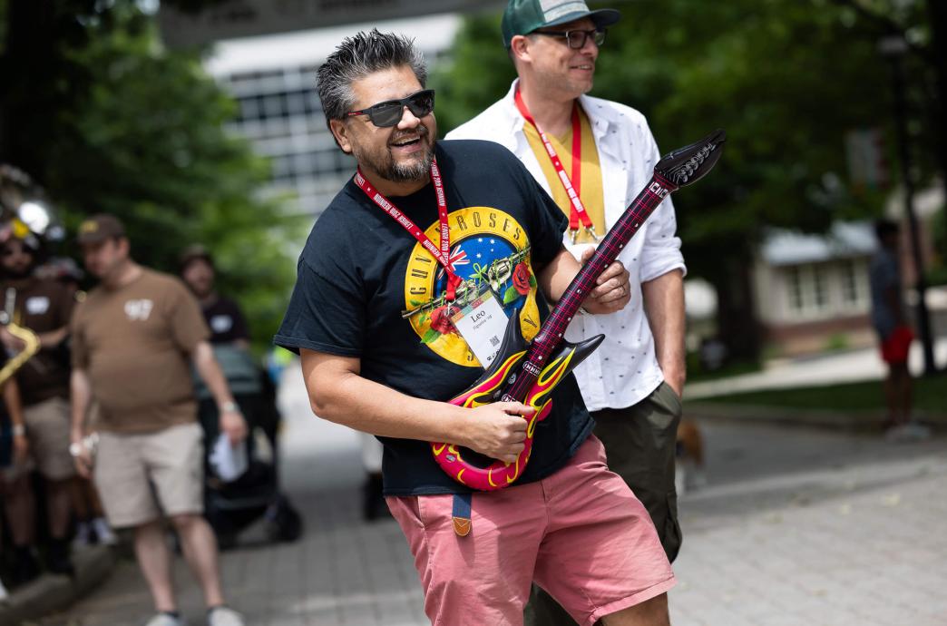 Man wearing sunglasses pretends to play an inflatable guitar while wearing a Guns N Roses shirt.