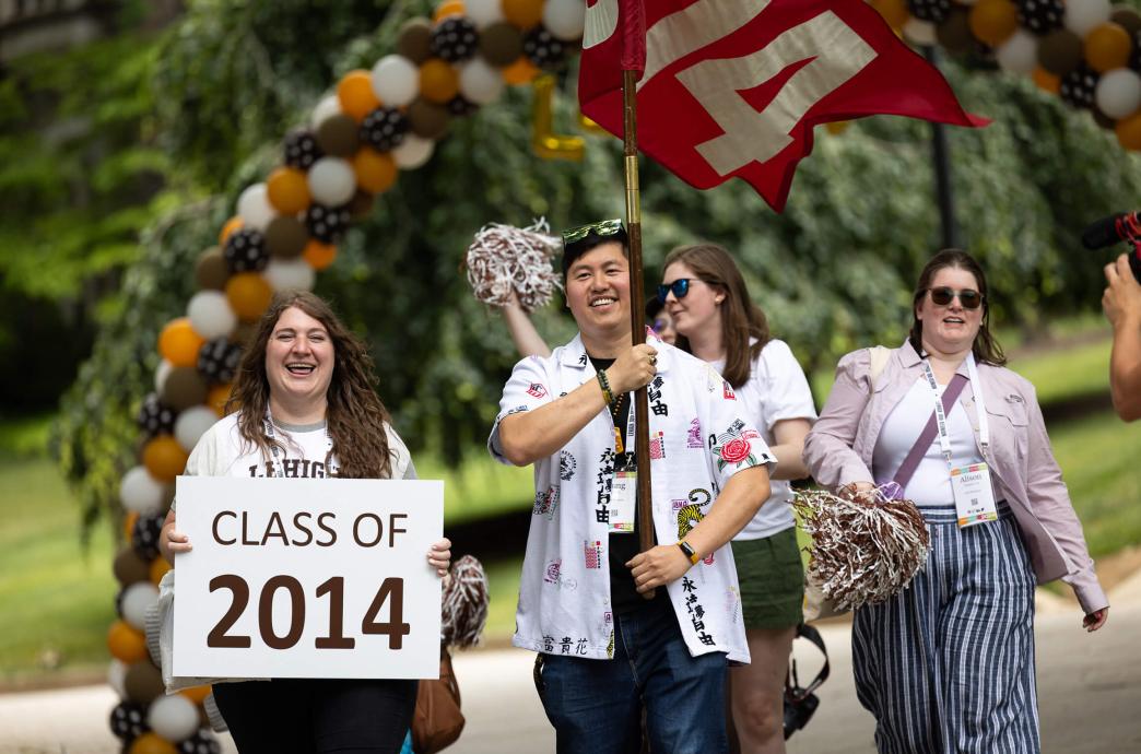 Alumni from the Class of 2014 parade at Reunion holding a flag, pompoms, and a sign with their class year.