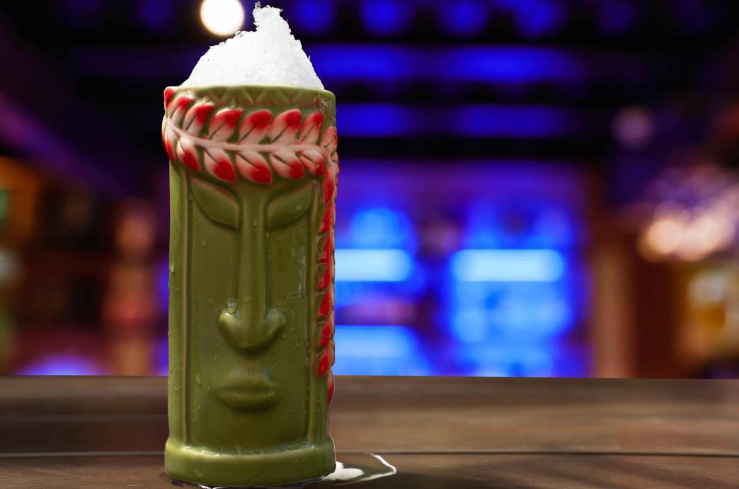 Green Face Tiki Mug sits on a bar with blue fluorescent lights in the background. 