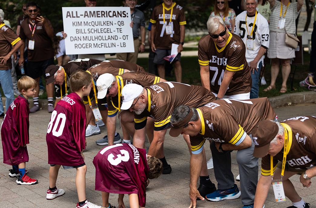 Men in Lehigh football jerseys line up in a football stance against children in Lafayette jerseys