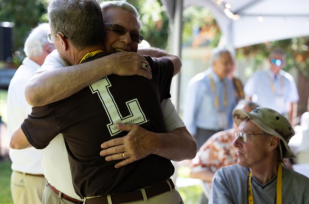 Two alumni embrace each other below a tent