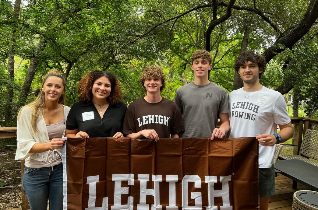 Students standing in front of green foliage while smiling and holding a brown Lehigh flag.