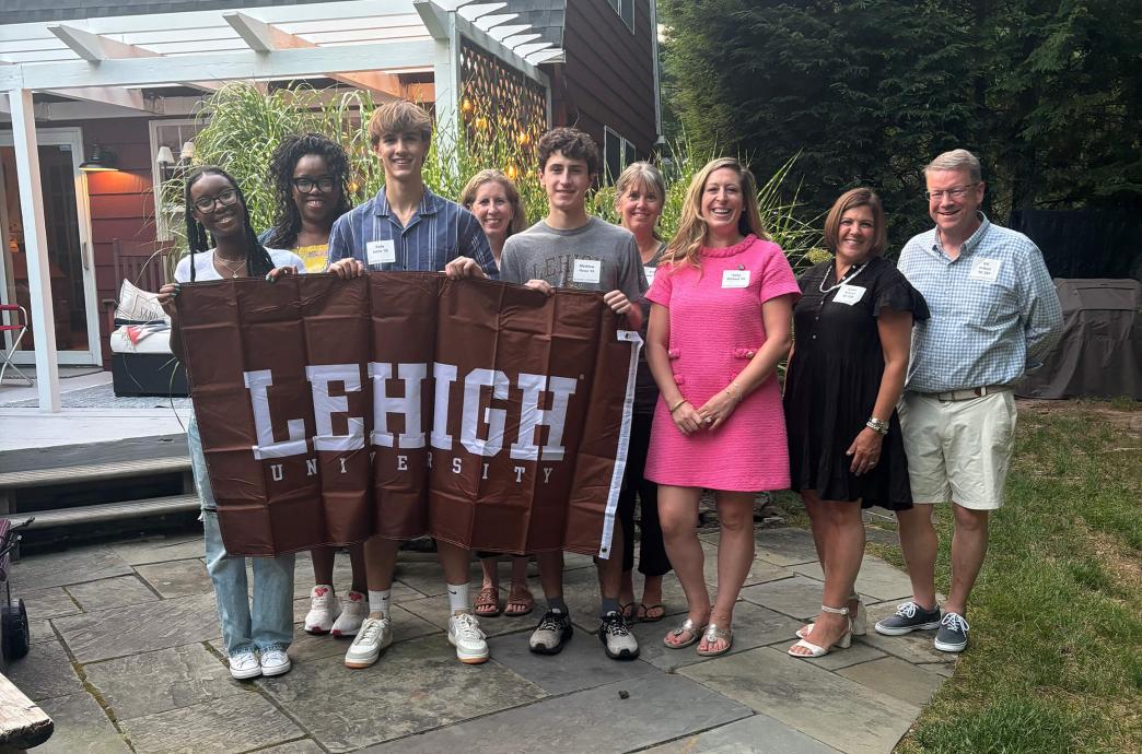 Students standing in front of a white pergola while smiling and holding a brown Lehigh flag.