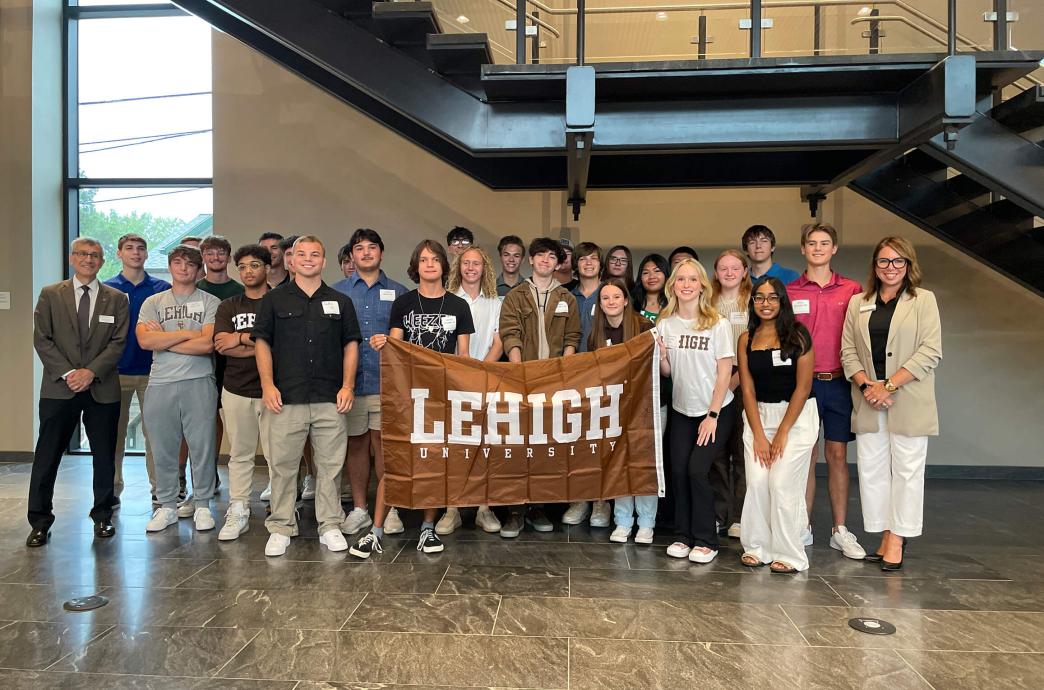 Students standing while smiling and holding a brown Lehigh flag.