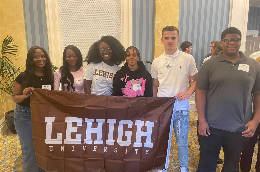 Students posed together in the home of an alumni while smiling and holding a brown Lehigh flag.