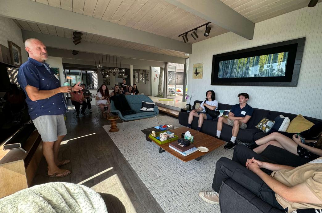 Students and an alumni lounging in a living room and chatting.