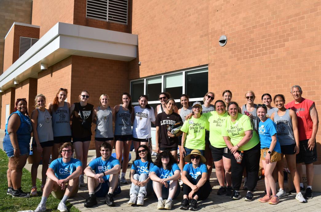 A group of volunteers pose outside on a sunny day, some standing behind others who are sitting for the photo..