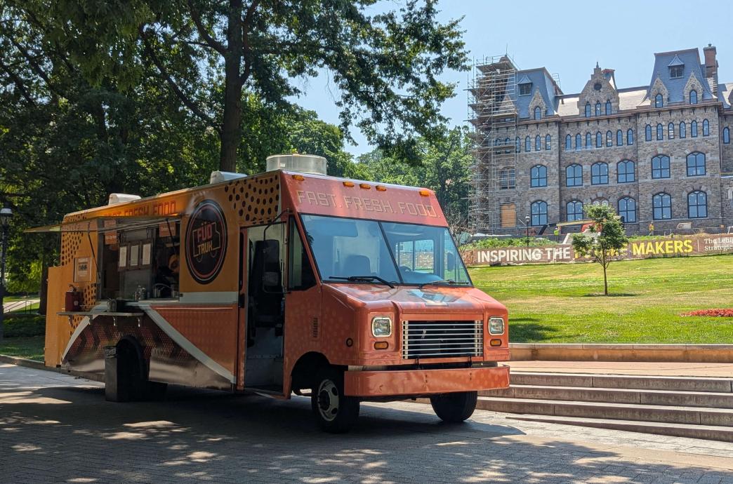 An orange food truck parked in front of the Clayton UC construction site.