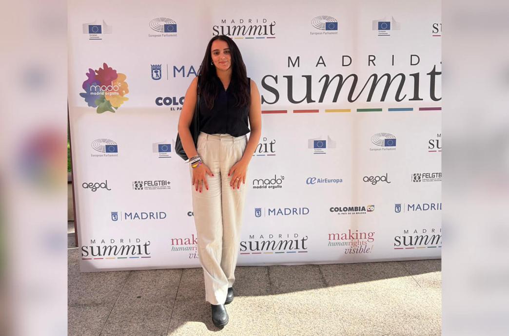A student poses in front of a step and repeat background for the Madrid Summit.