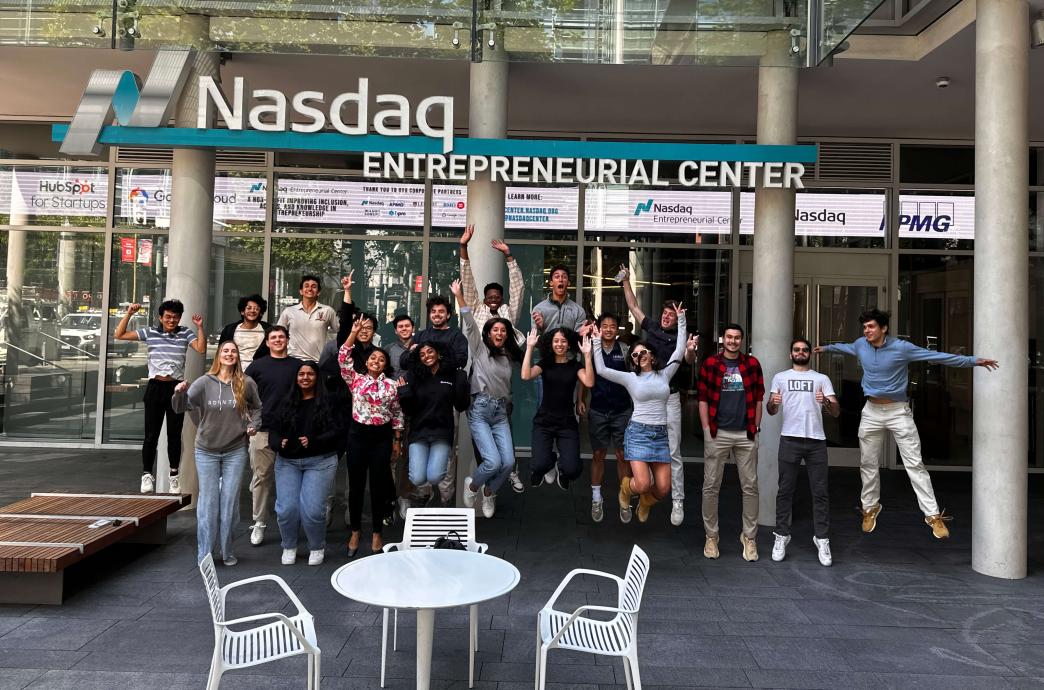 A group of students literally jump for joy in front of the Nasdaq Entrepreneurial Center sign.