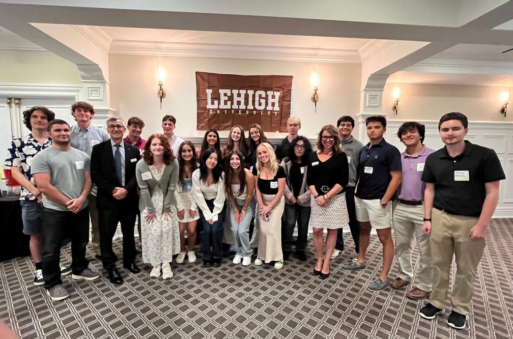 Students gather inside for a photo while holding a brown Lehigh University flag.