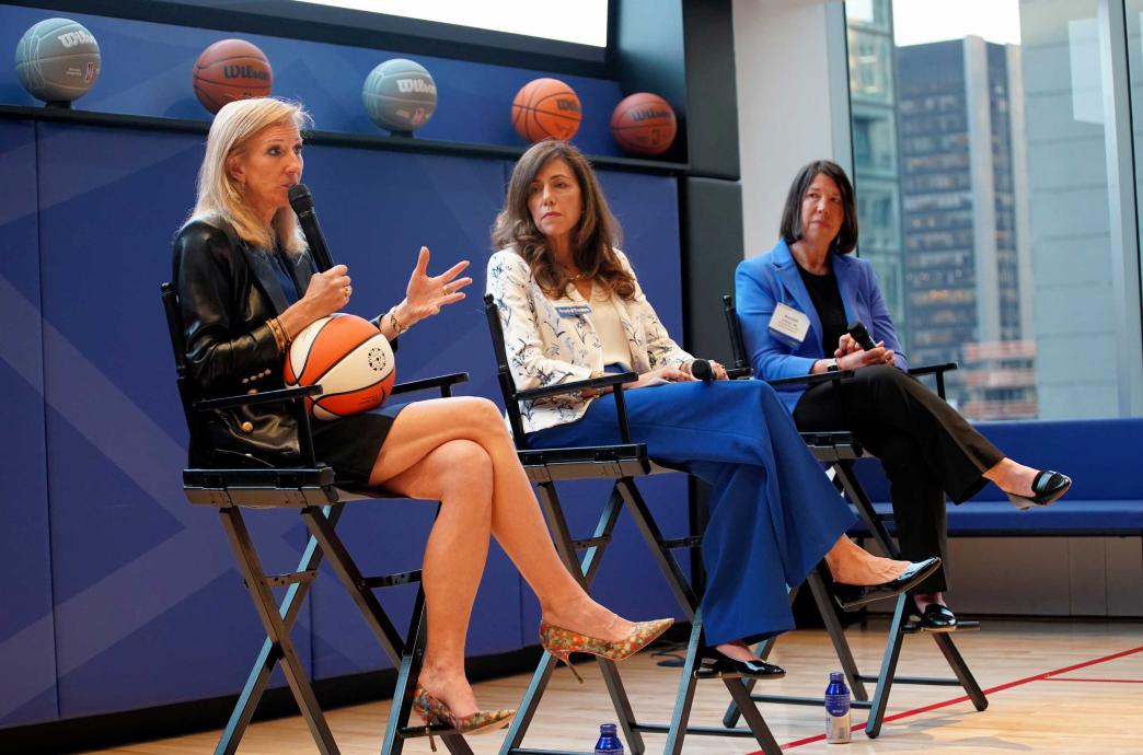three women sitting on tall chairs on a basketball court