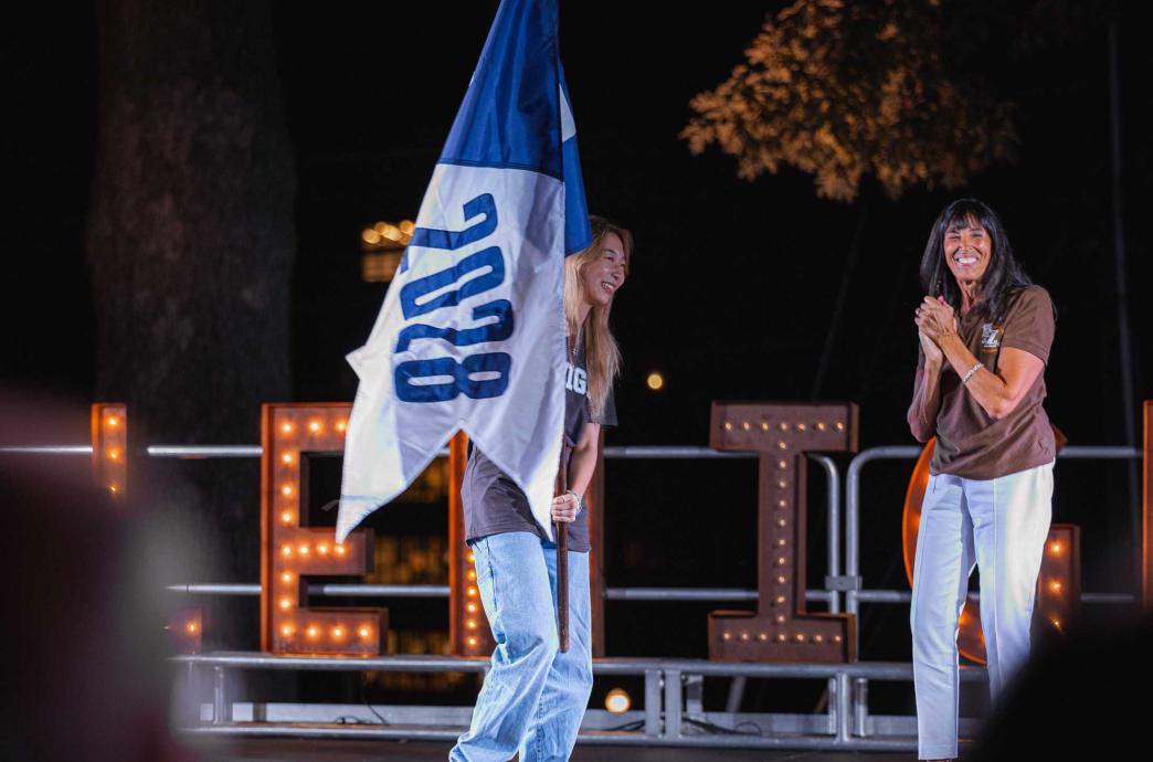 Two women on stage to represent their class and hold their class flags.