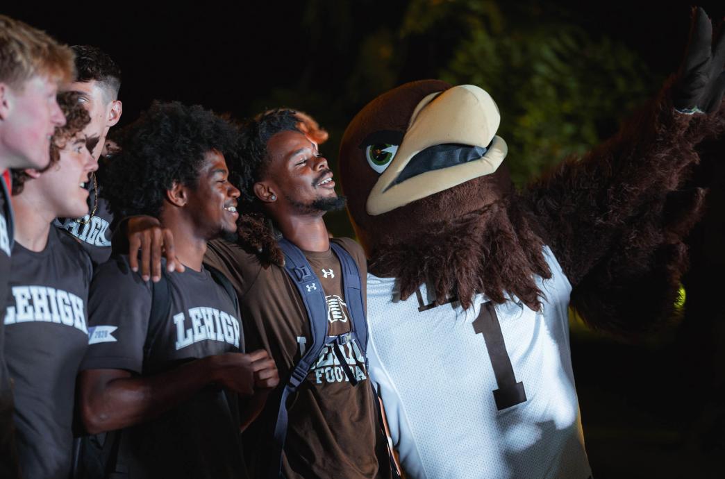 Mountain Hawk mascot, Clutch, puts one arm around students wearing brown Lehigh t-shirts.