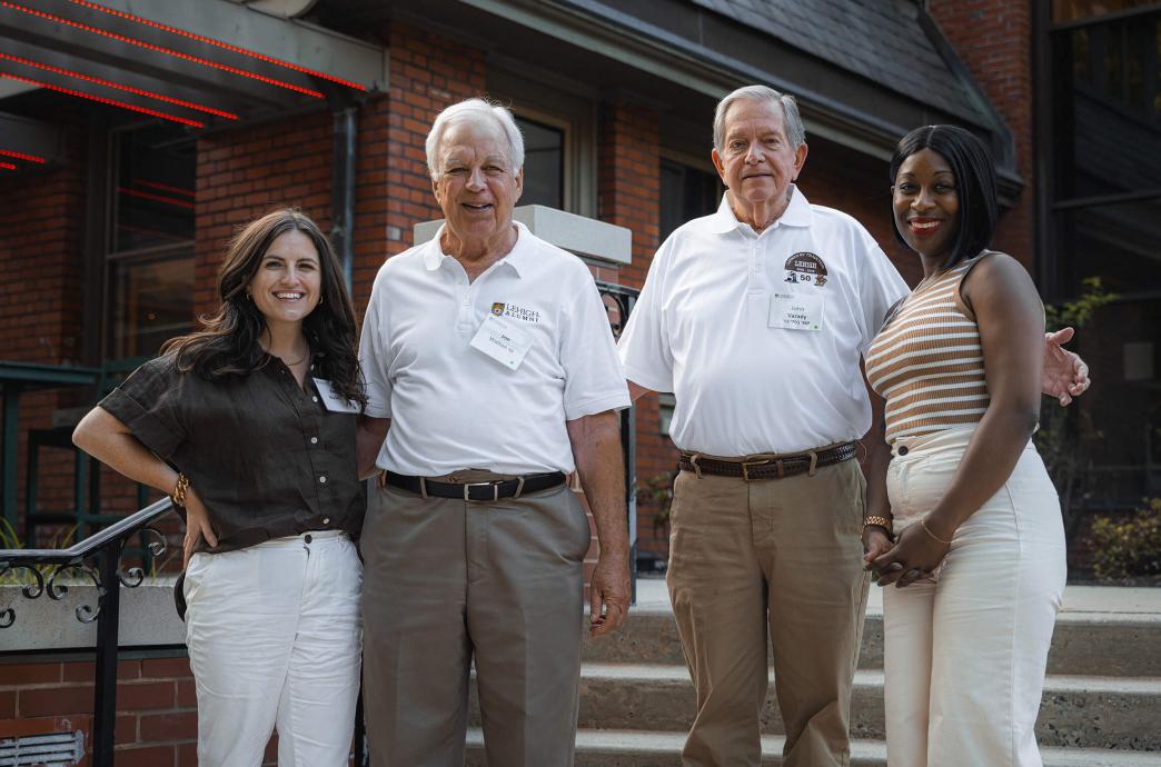 Four people stand side-by-side outside an alumni event for a group photo.