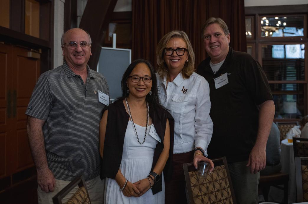 Four alumni stand side-by-side at an alumni event and pose for a group photo.