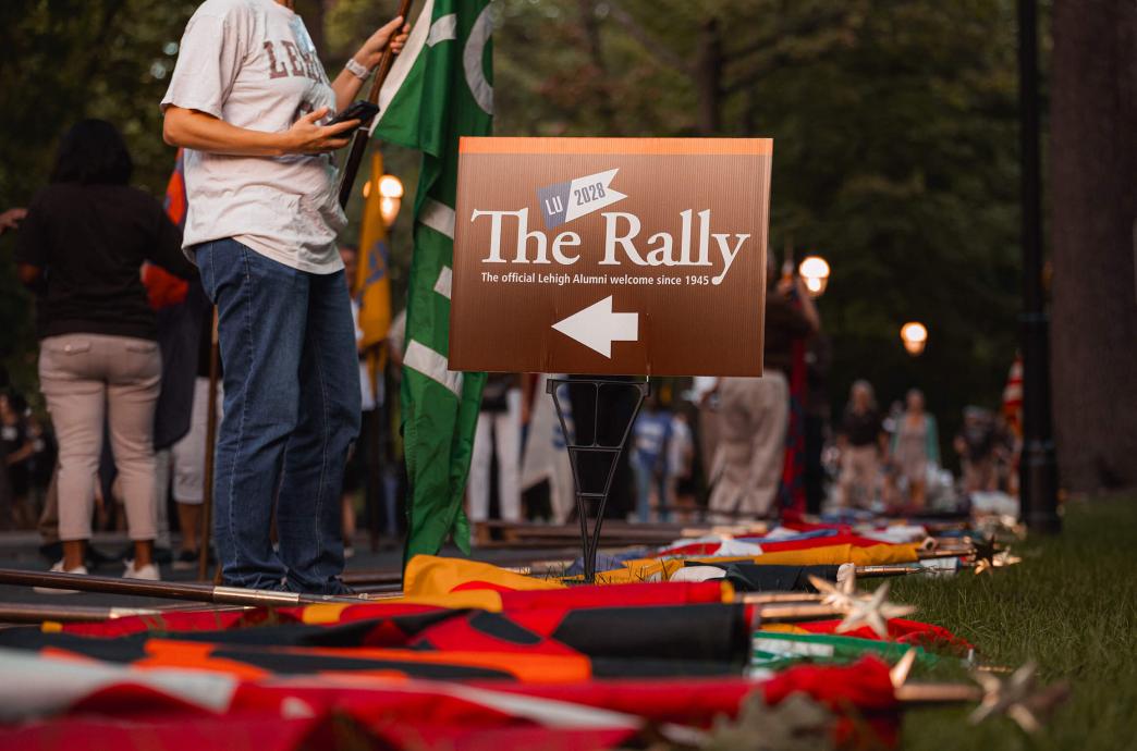 A sign reading "The Rally: The first Official Lehigh Welcome since 1945" stuck in the grass with colored flags lying on the ground.