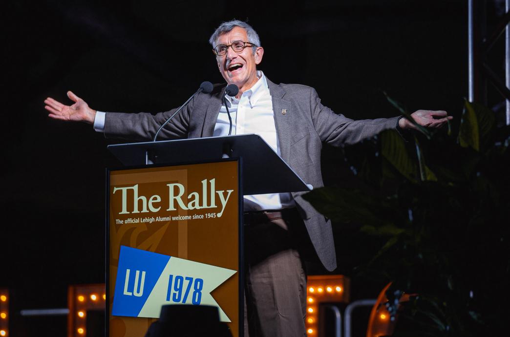 Lehigh University president, Joe Helble, stands at a podium that reads "The Rally" with his arms outstretched.