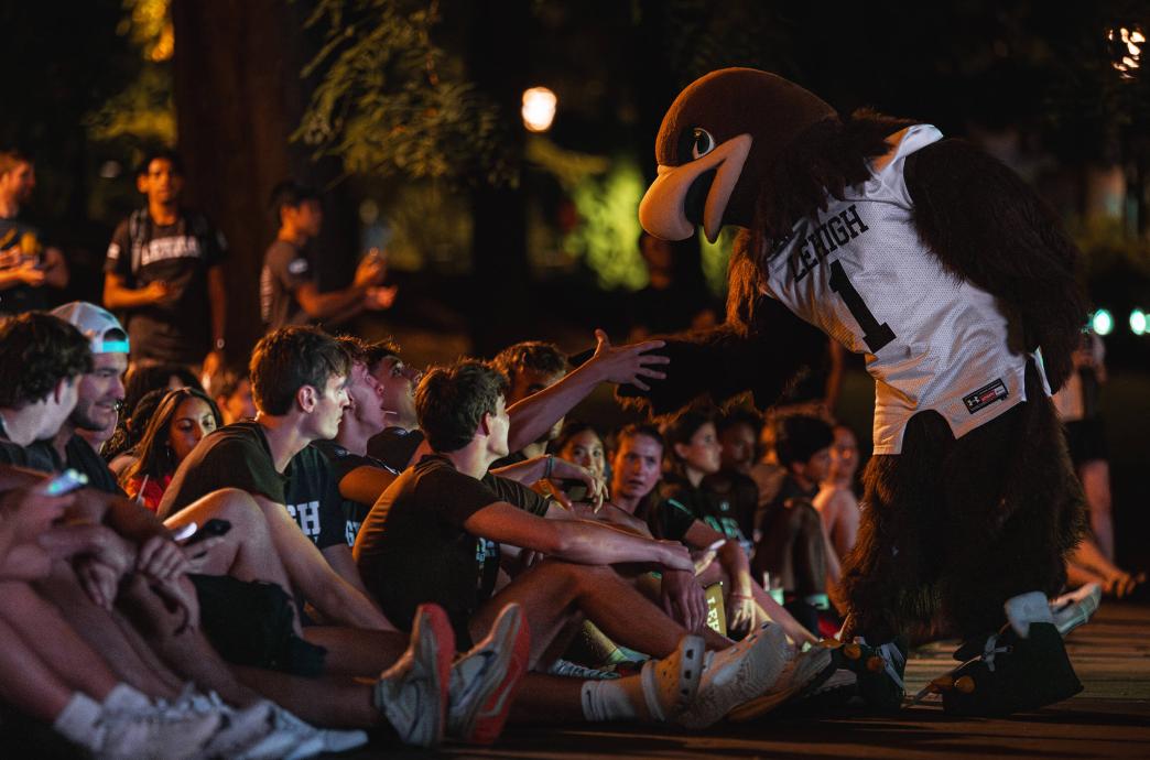 Lehigh Mountain Hawk mascot, Clutch, bends to greet students sitting on the ground at Rally.