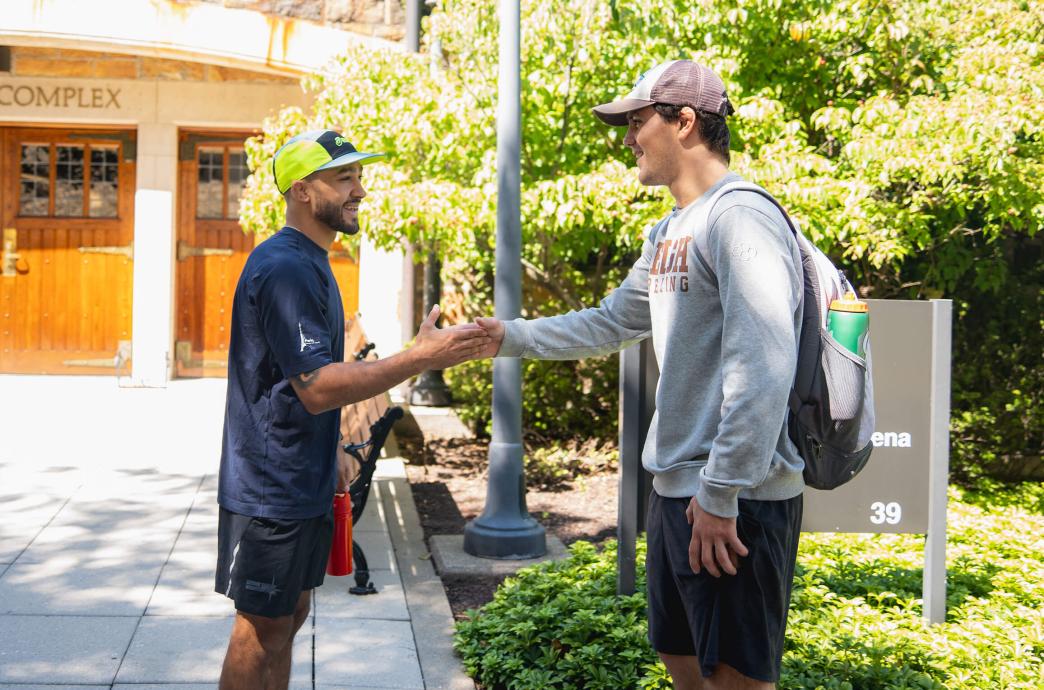 Darian Cruz shakes hands with a student outside the Caruso Complex on a bright sunny day.