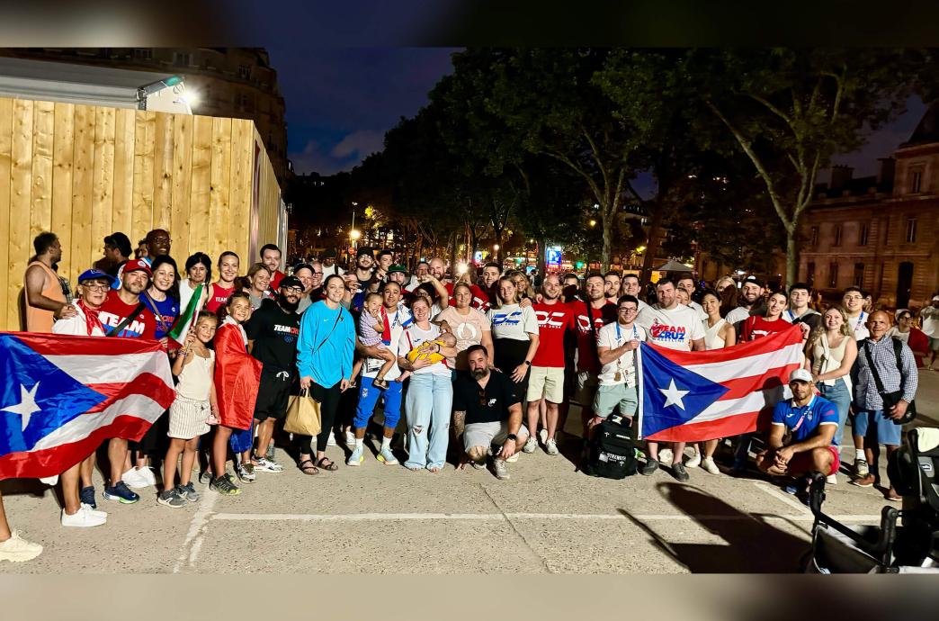 Darian Cruz stands outside in the night with a crowd of supporters beside him holding Puerto Rican flags.