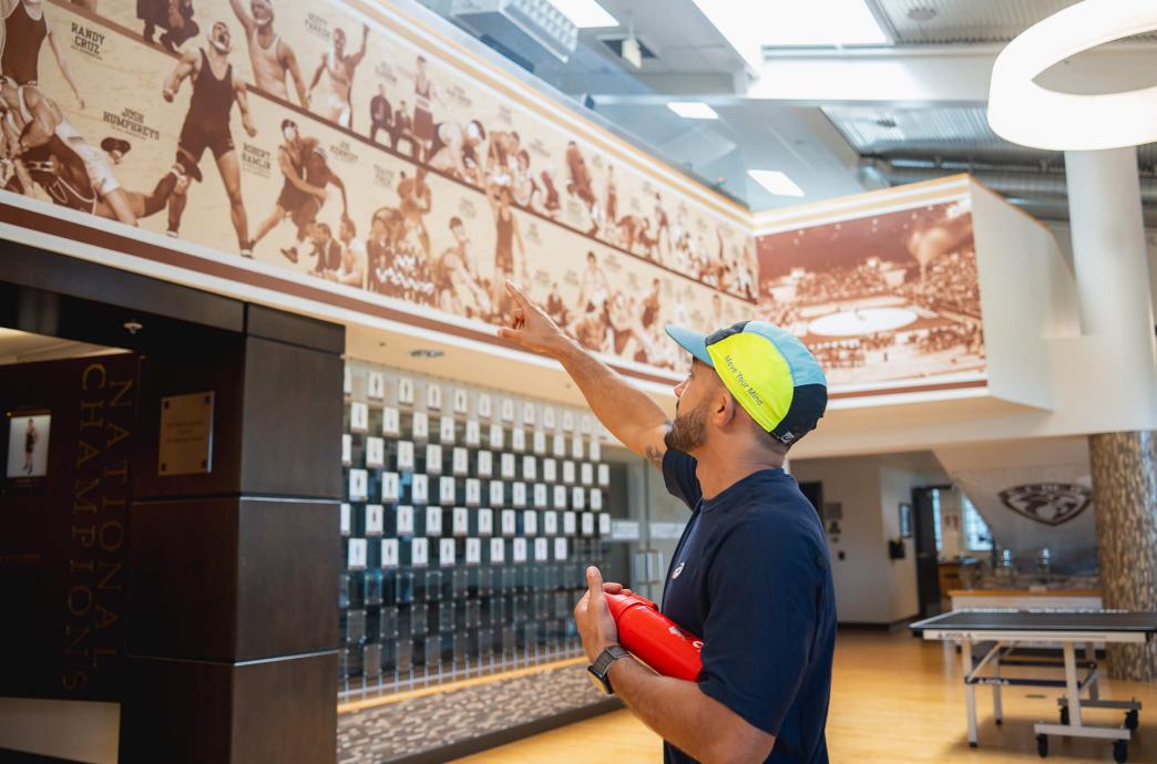 Darian Cruz stands inside Grace Hall and points to a mural of Lehigh standouts, including his brother, Randy.