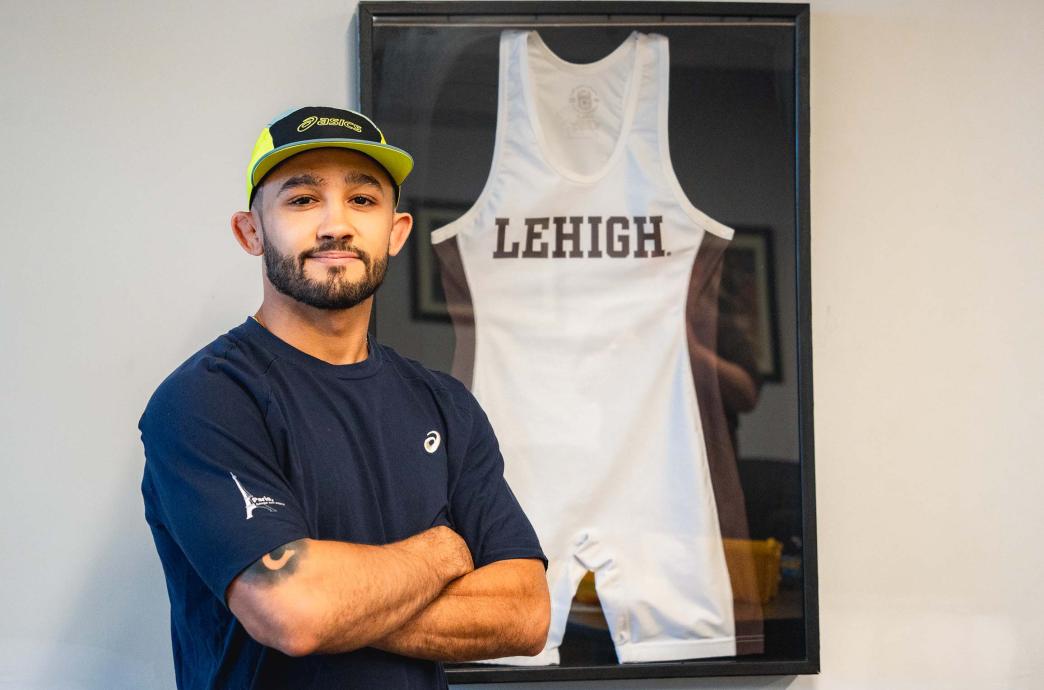 Darian Cruz poses beside a framed Lehigh Wrestling singlet.