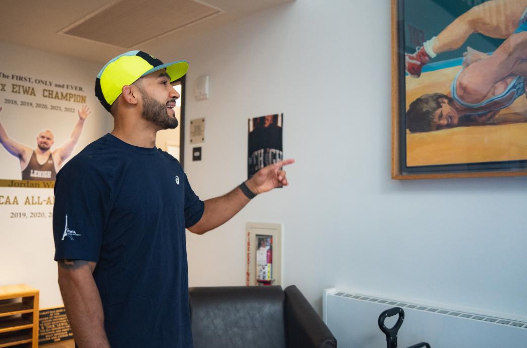 Darian Cruz points and smiles at wall art depicting 2 wrestlers.