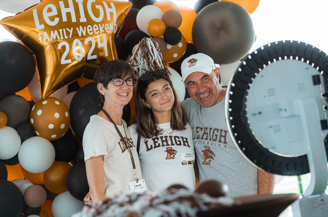 Mother and father pose with their daughter at a photo booth, all wearing Lehigh shirts.