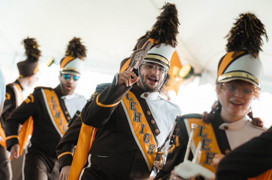 A row of band members process in a line, with one raising a small, brown, foam finger in the air.