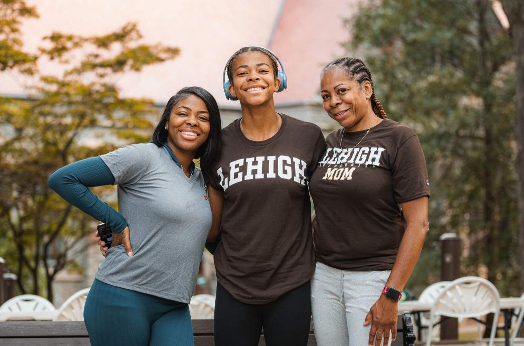 A student stands between two female family members, wearing a Lehigh shirt beside their mother in a “Lehigh Mom” t-shirt.
