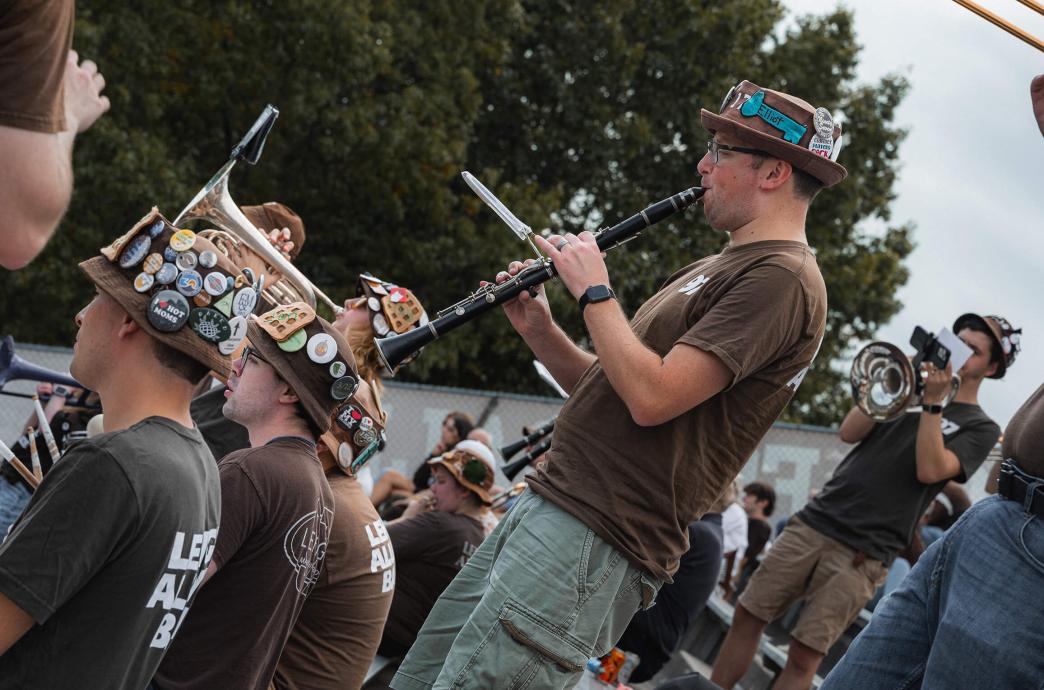 Wearing bucket hats adorned with buttons and brown t-shirts reading “Lehigh Alumni Band,” the alumni band plays in the stands. 