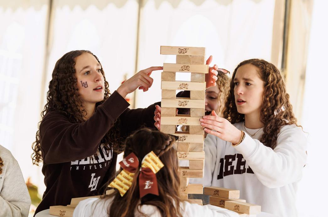 Two young female attendees wearing Lehigh sweatshirts carefully play a game of Jenga at a hightop table.