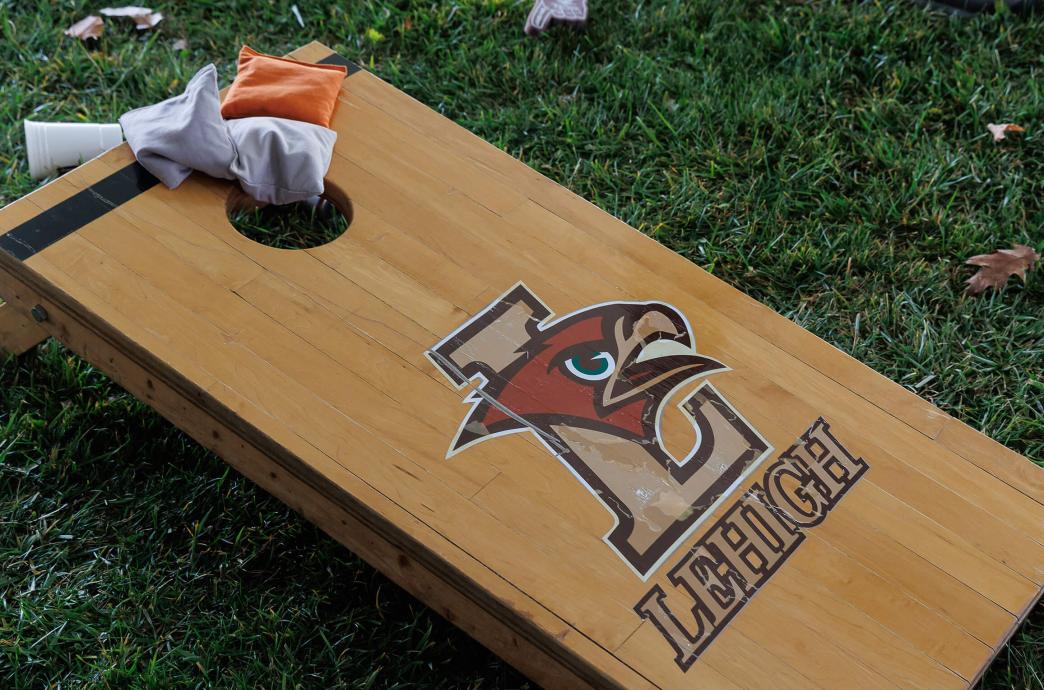 A wooden baggo board emblazoned with the Mountain Hawk logo sits on the grass with bean bags resting on the top of the board.