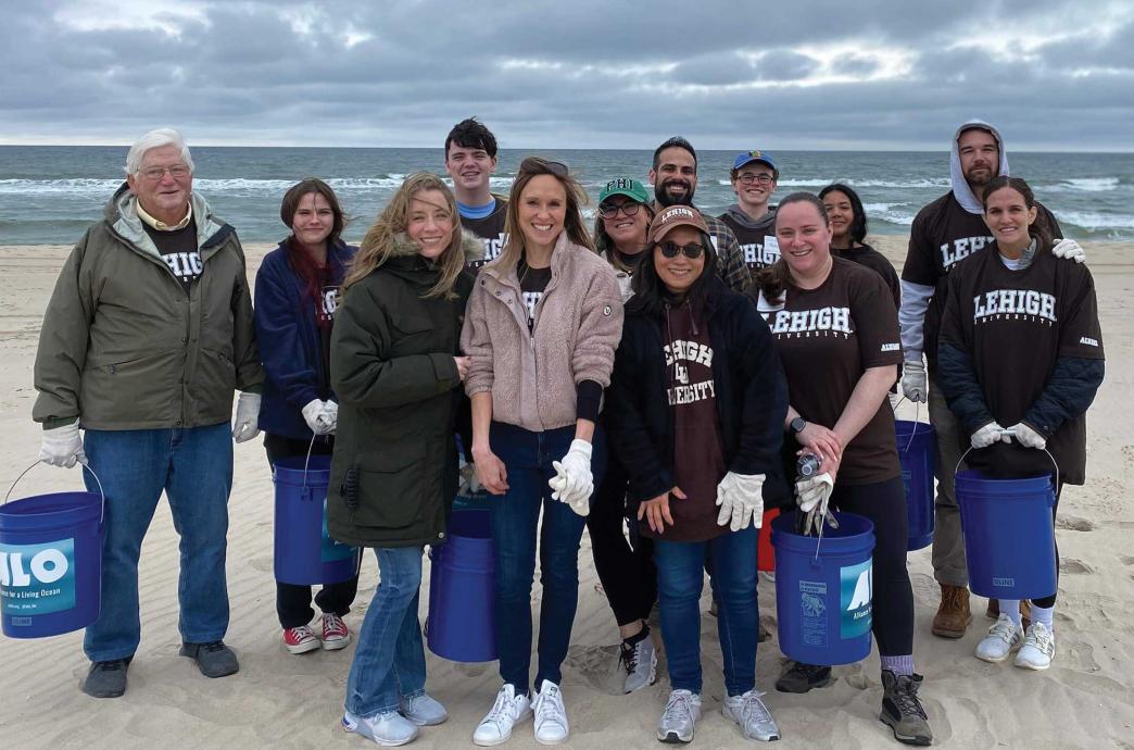 A Group stands on a beach, carrying buckets and wearing brown and white Lehigh gear.
