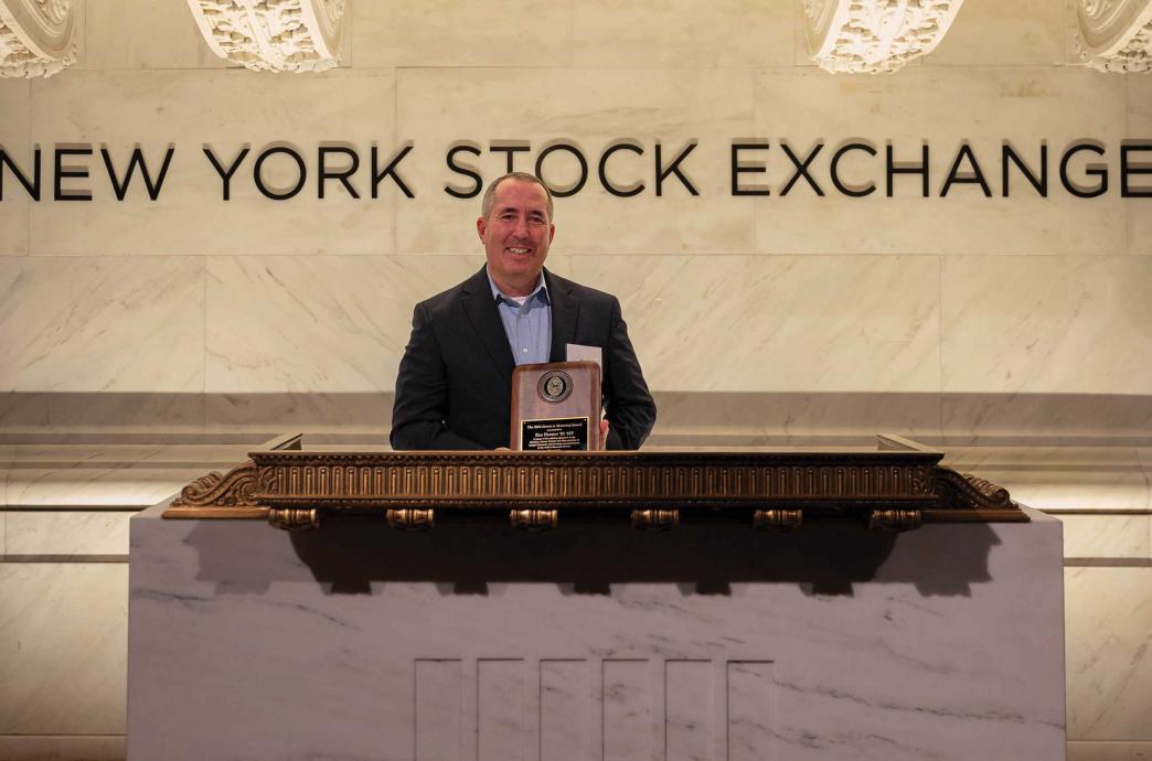 Ken Hoexter holding his award while standing behind a podium at the New York Stock Exchange.
