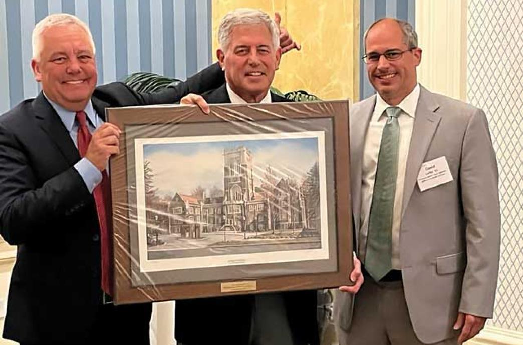 Three men stand together holding a painting of the Alumni Memorial Building.
