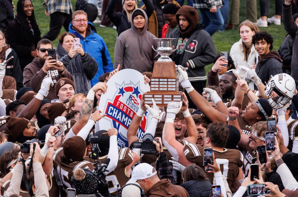 Lehigh football players holding their trophy above their heads, next to a sign reading "Patriot Football League Champions."