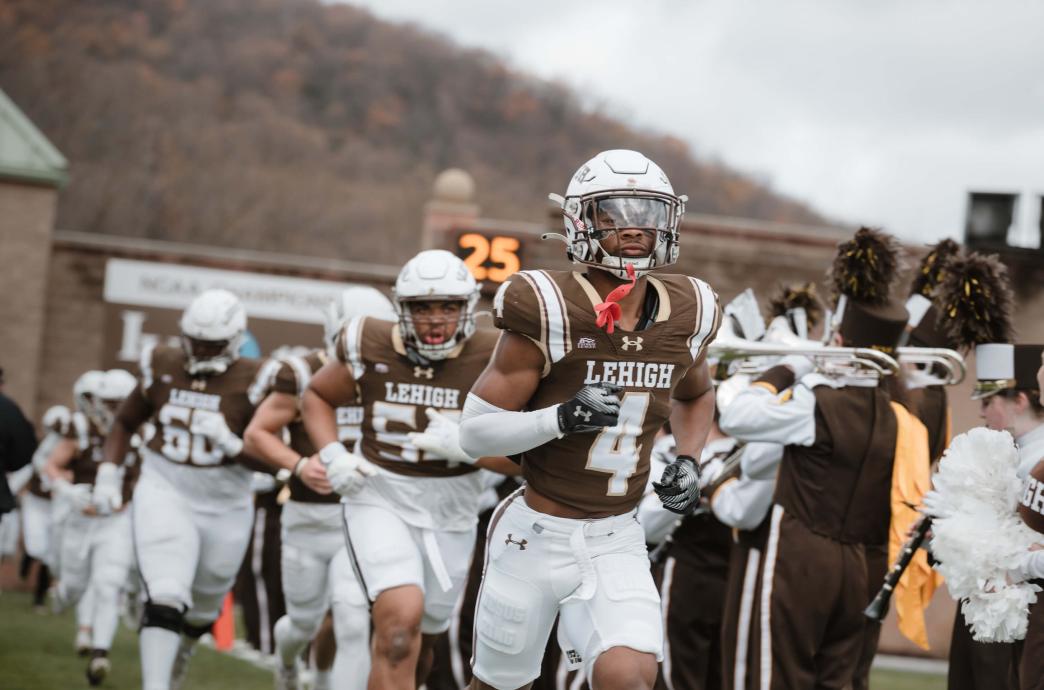 A few football players running onto the field between the lines of the Lehigh Band.