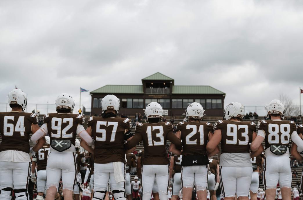 Football players photographed from behind while wearing their brown and white gear.