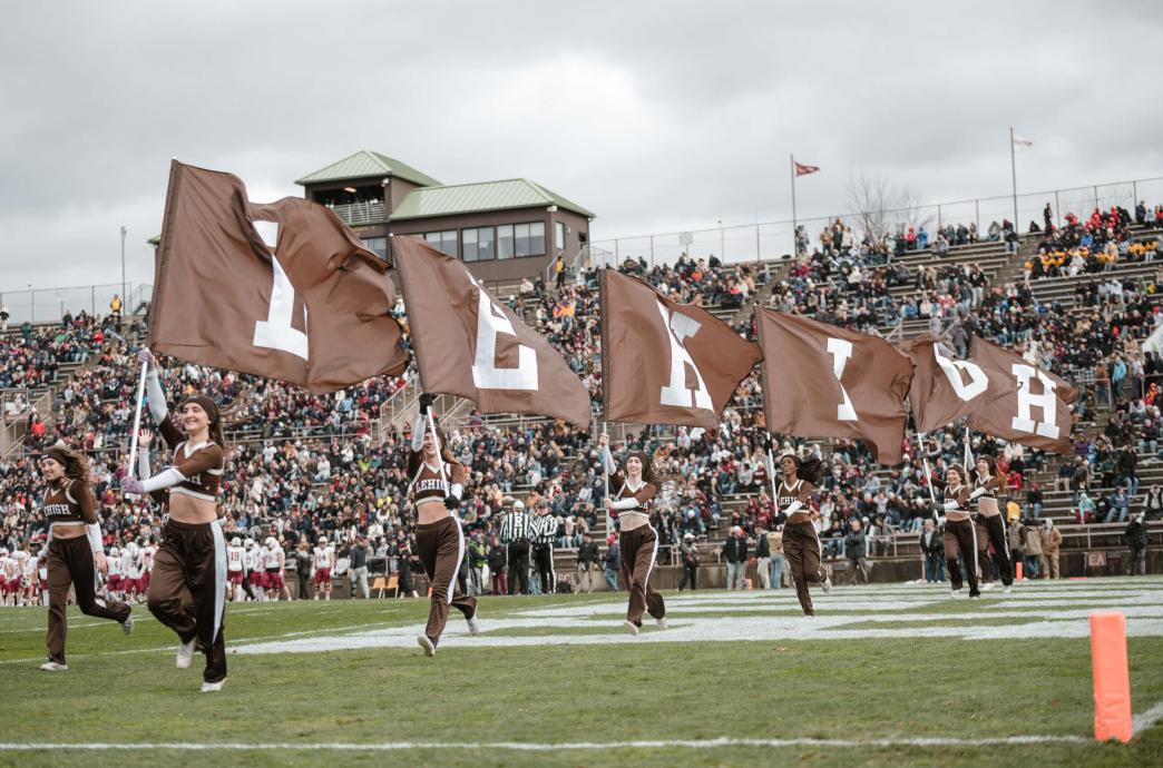 Cheerleaders running with brown flags with white letters. The flags read "Lehigh."