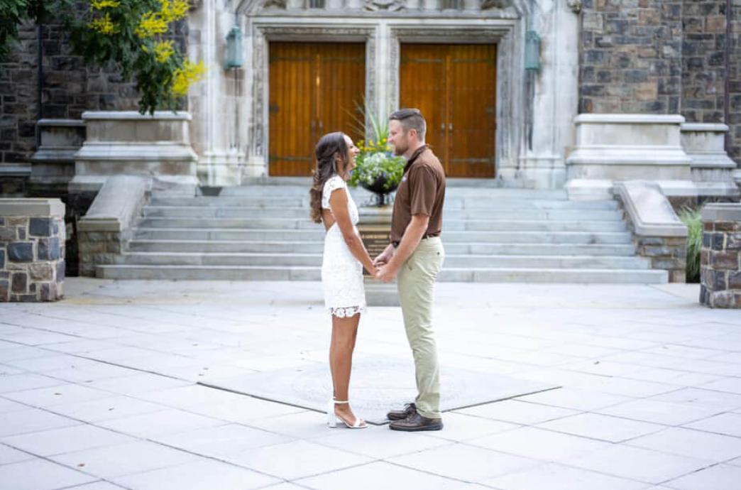 A couple stands on campus of Lehigh while facing each other, the woman wearing white and the man wearing a brown polo shirt.