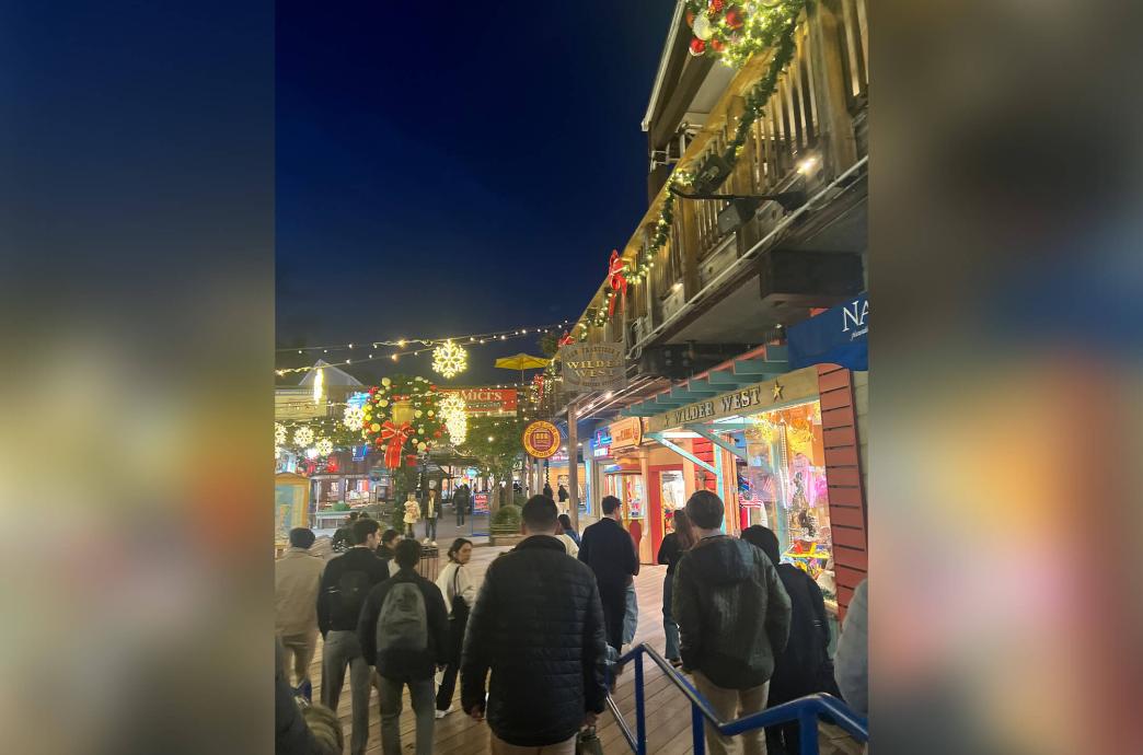 A night view of Pier39 in San Francisco with people strolling down the pier and lights hanging above them.