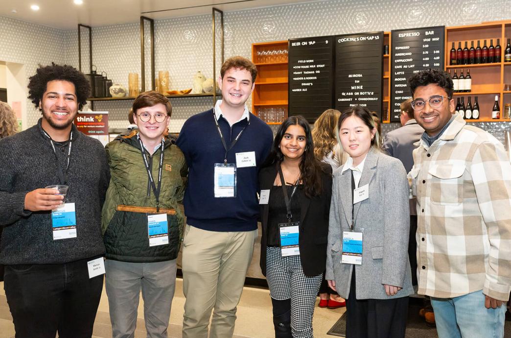 Six students stand at an event dressed casually with lanyards around their necks.