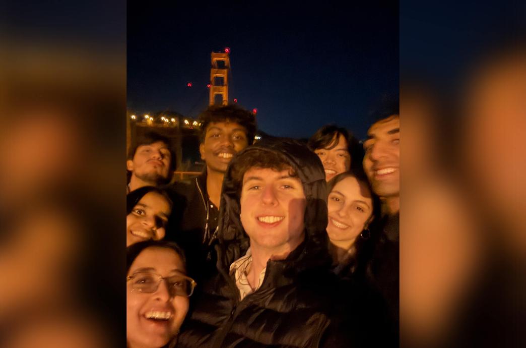 A group of students pose for a selfie in front of the Golden Gate Bridge at night.