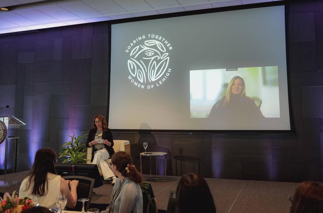 Carol Packard sits on the stage with a large projection behind her featuring Brooke Eby.