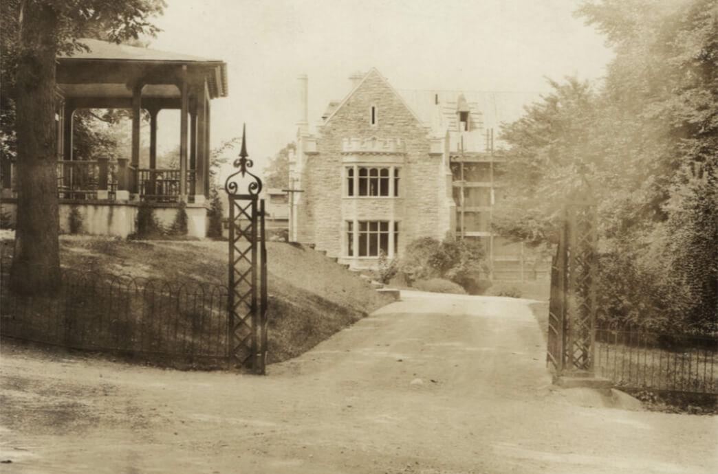 Old photo of the construction of a stone building featuring a gated entrance, showcasing classic architecture.